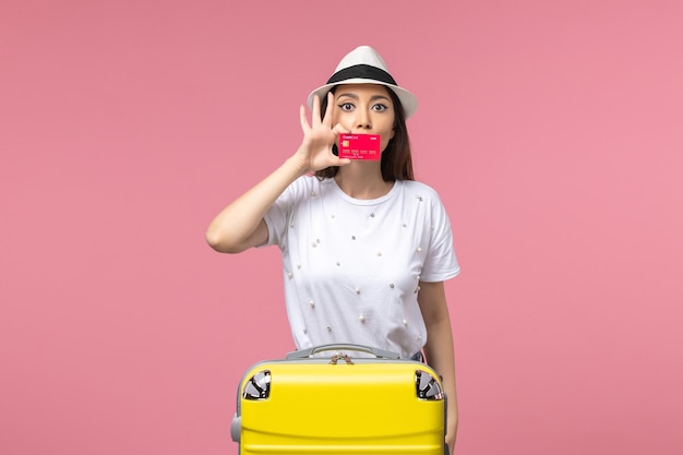 淡いピンクの壁の航海の夏の旅行で赤い銀行カードを保持している正面図若い女性