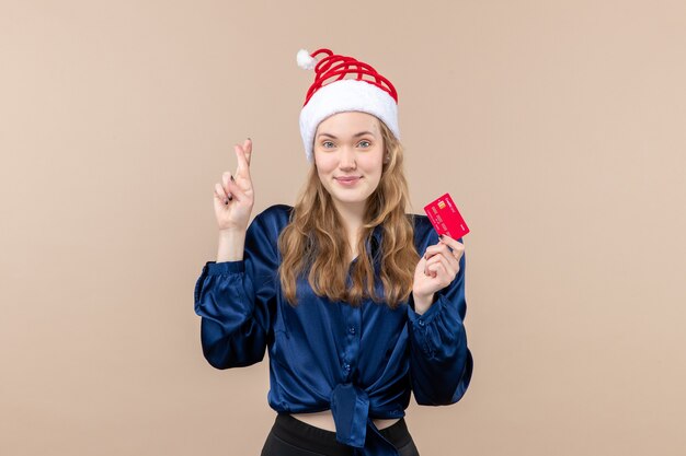 ピンクの背景に赤い銀行カードを保持している正面図若い女性休日クリスマスお金写真新年の感情
