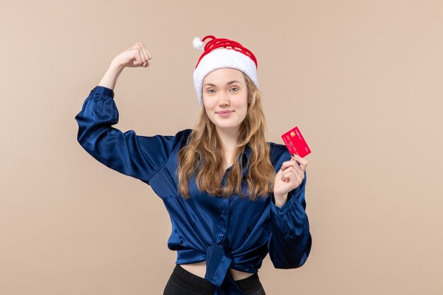Вид спереди молодая женщина держит красную банковскую карту на розовом фоне праздник рождественские деньги фото новогодние эмоции