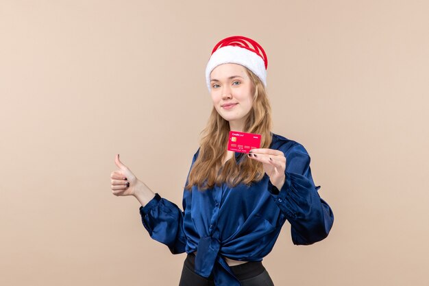 ピンクの机の上の赤い銀行カードを保持している正面図若い女性休日の写真新年クリスマスのお金の感情
