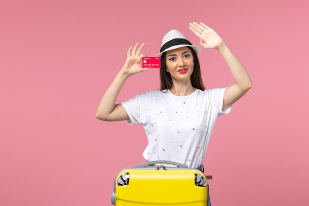 Front view young female holding red bank card on pink desk summer voyage trip color