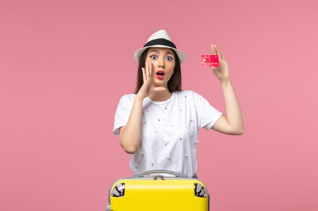 Front view young female holding red bank card on the pink wall color trip summer voyage