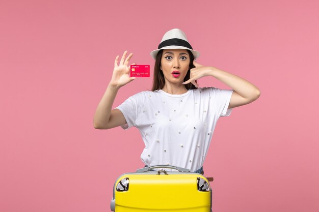 Front view young female holding red bank card on a pink wall summer trip voyage