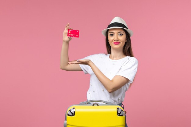 Front view young female holding red bank card on pink wall summer trip voyage