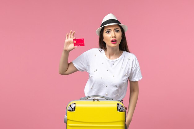 Front view young female holding red bank card on pink wall summer voyage trip color