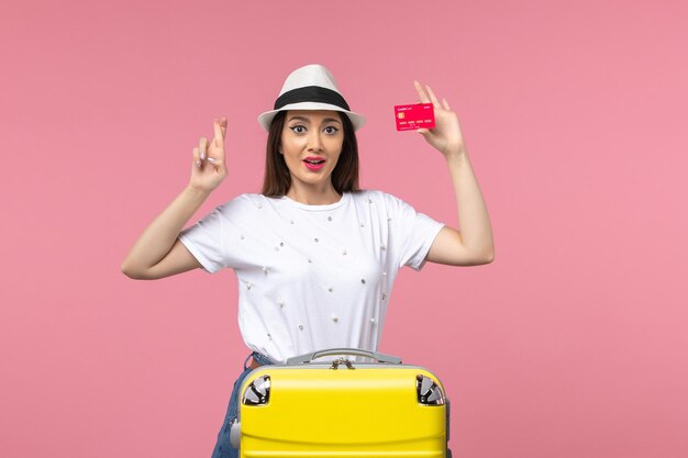 Front view young female holding red bank card on pink wall voyage color trip summer