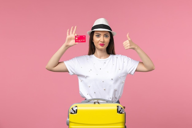 Front view young female holding red bank card on a pink wall voyage summer trip