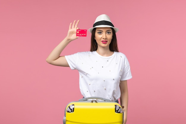 Front view young female holding red bank card on pink wall voyage summer trip