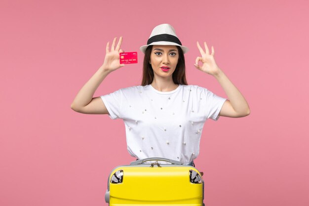 Front view young female holding red bank card on the pink wall voyage summer trip