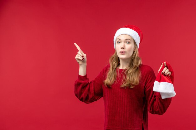 Вид спереди молодая женщина, держащая красную кепку на красном полу, праздник рождества