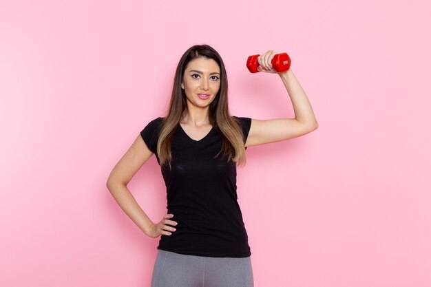 Front view young female holding red dumbbells on light pink desk athlete sport exercise health workouts
