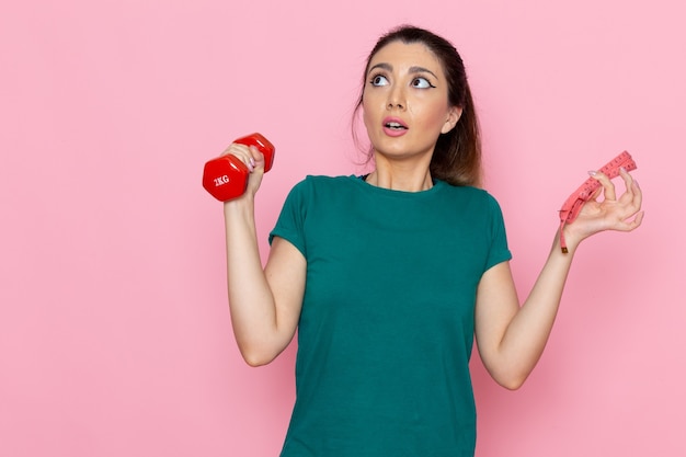 Front view young female holding red dumbbells on light-pink wall athlete sport exercise health workouts