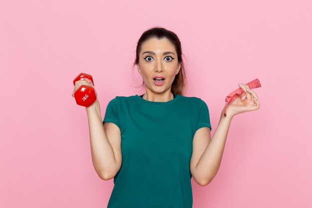 Front view young female holding red dumbbells on the light pink wall athlete sport exercise health workouts