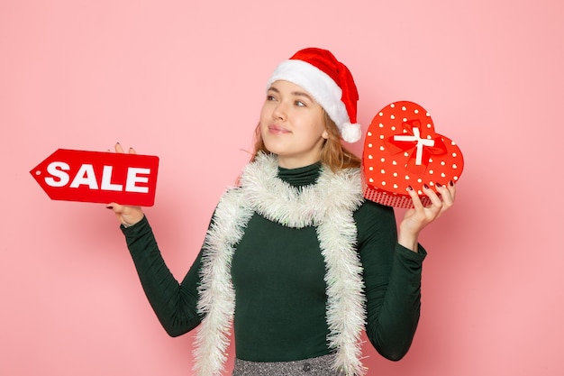 Free photo front view young female holding red sale writing and present on pink wall christmas new year emotion holiday