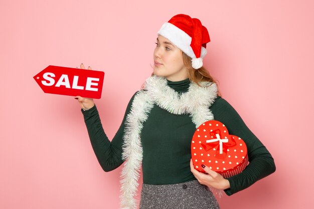 Front view young female holding red sale writing and present on pink wall christmas new year shopping emotion holiday color