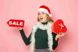 Free photo front view young female holding red sale writing and present on pink wall christmas new year shopping emotions holiday