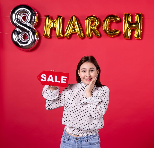 Front view young female holding sale nameplate on march decorated red background feminine beauty holiday passion equality affectionate woman horizontal lover