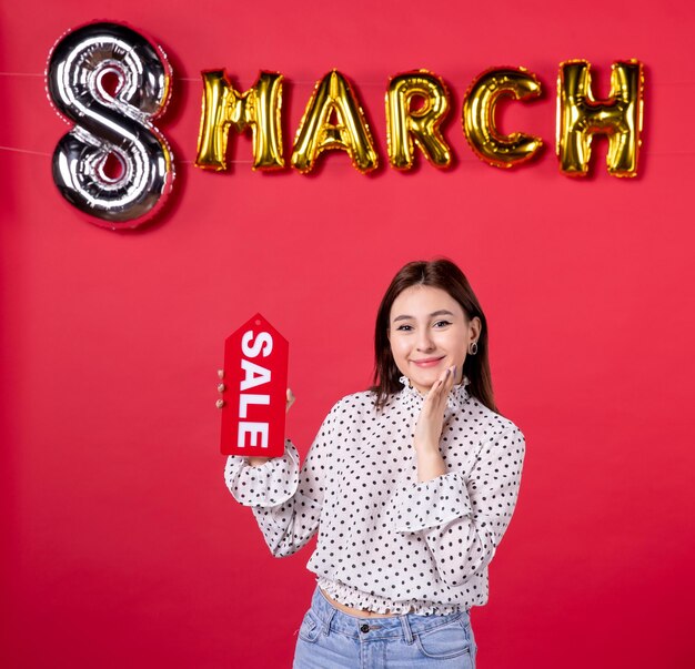 Front view young female holding sale nameplate on march decorated red background passion love feminine holiday affectionate horizontal beauty equality