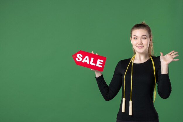 Вид спереди молодая женщина, держащая распродажу, писать на зеленом