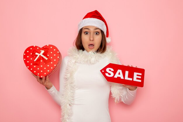 Front view young female holding sale writing and present on pink wall color fashion holidays new year snow christmas