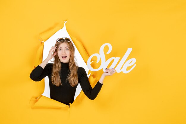 Front view young female holding sale writing through torn paper hole in the wall