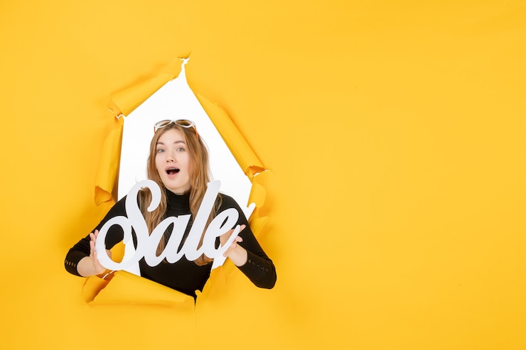 Free Photo front view young female holding sale writing through torn paper hole in the wall