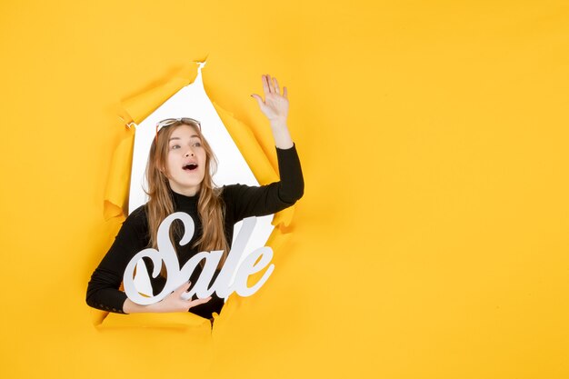 Front view young female holding sale writing through torn paper hole in the wall