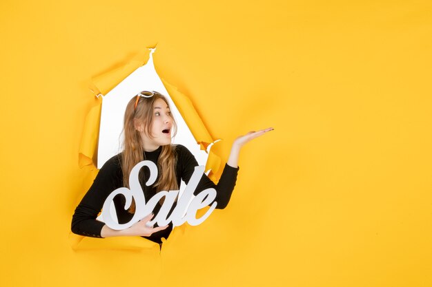 Front view young female holding sale writing through torn paper hole in the wall