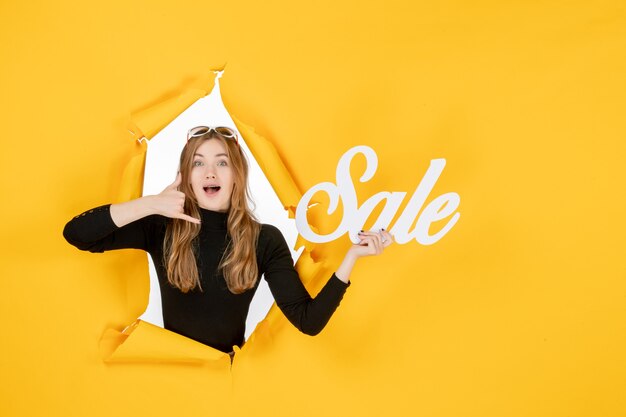 front view young female holding sale writing through torn paper hole in the wall