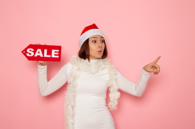 Front view young female holding sale written figure on the pink wall color christmas new year holiday fashion snow