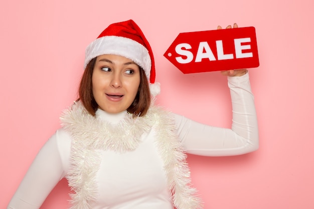 Free photo front view young female holding sale written figure on pink wall color holiday new year fashion snow christmas