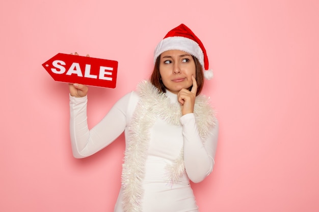 Free photo front view young female holding sale written figure thinking on pink wall holiday christmas new year fashion snow color