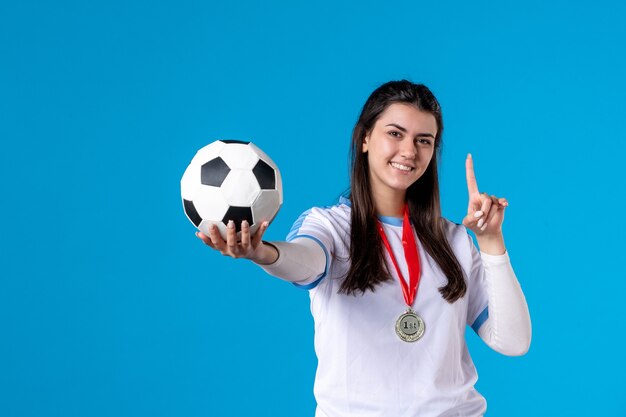 Вид спереди молодая женщина держит футбольный мяч на синей стене
