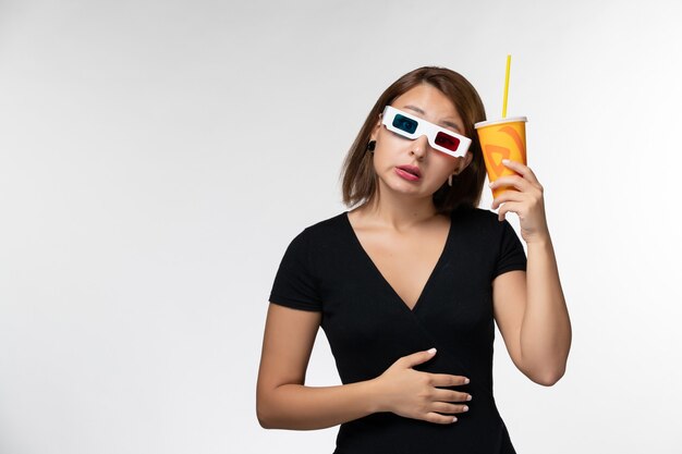 Вид спереди молодая женщина, держащая газировку в солнцезащитных очках d на белой поверхности