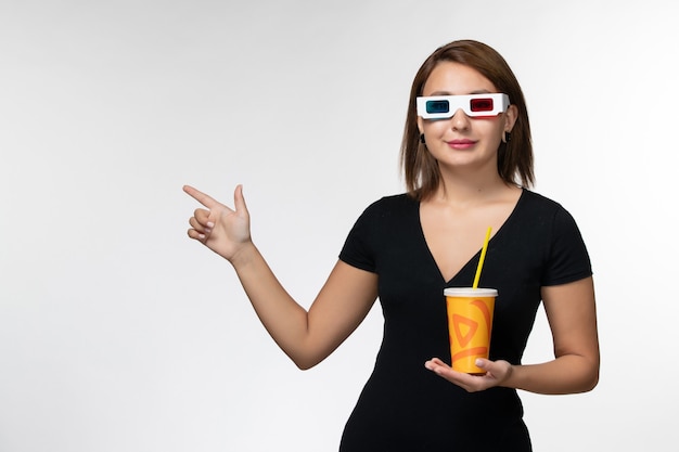 Vista frontale della giovane donna che tiene la soda in occhiali da sole d con il sorriso sulla superficie bianca