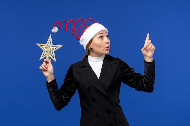 Free photo front view young female holding star shaped toy on blue wall holiday new year eve