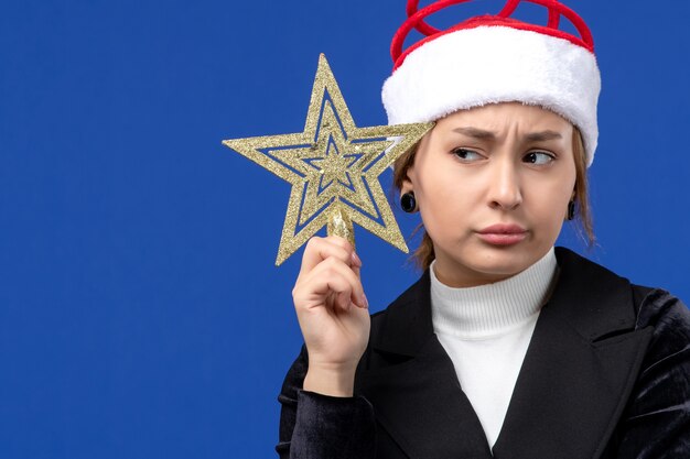 Front view young female holding star shaped toy on a blue wall holidays new year eve