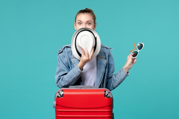 Front view young female holding sunglasses and hat preparing for vacation on blue space