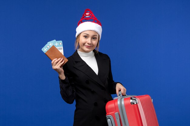 Вид спереди молодая женщина, держащая билеты с сумкой на синем фоне, женщина, отпуск, праздник