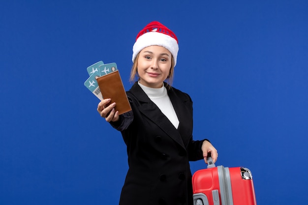 Вид спереди молодая женщина, держащая билеты с сумкой на синем столе, праздники, самолет, отдых