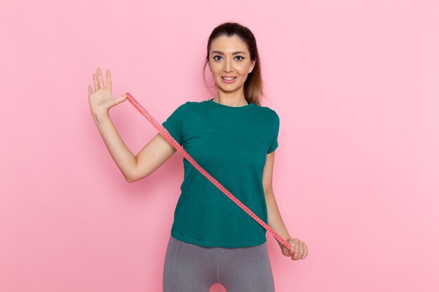 Front view young female holding waist measure on the pink wall beauty sport exercise athlete workout slim