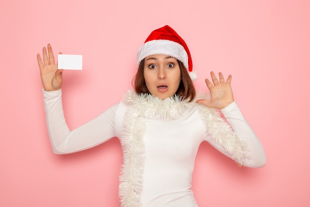正面図ピンクの壁に白い銀行カードを保持している若い女性クリスマス色休日新年ファッション