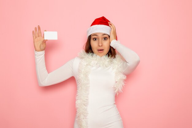 Front view young female holding white bank card on pink wall christmas holiday new year color money