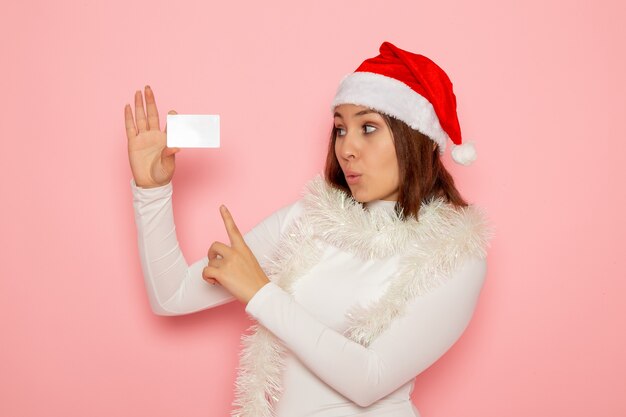 Front view young female holding white bank card on pink wall christmas new year fashion color holiday