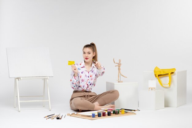 Front view young female holding yellow bank card on the white background