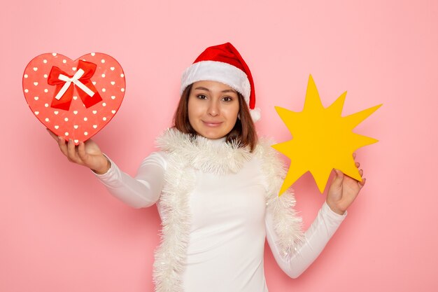 Front view young female holding yellow figure and present on the pink wall christmas color holiday new year fashion