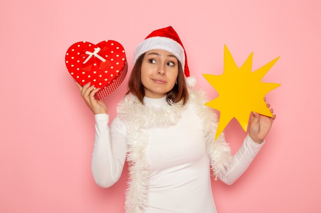 Front view young female holding yellow figure and present on the pink wall snow christmas color holiday new year fashion