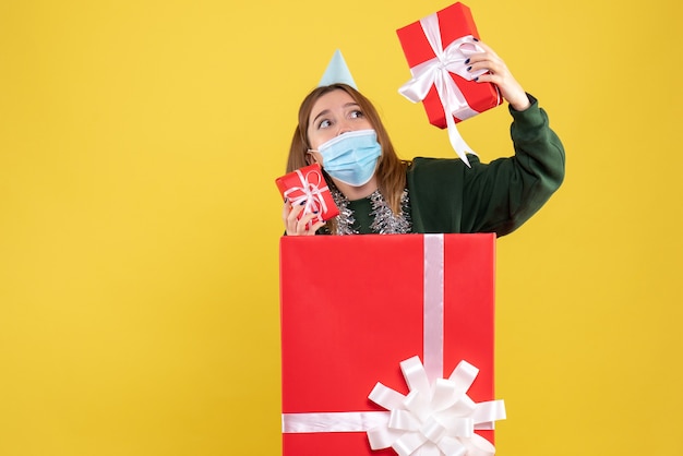 Вид спереди молодой женщины внутри подарочной коробки в стерильной маске с подарками