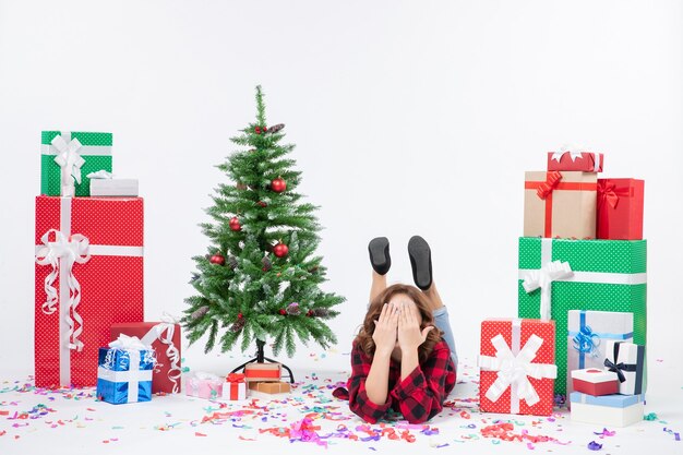 Вид спереди молодая женщина, лежащая вокруг рождественских подарков и праздничной елки на белом фоне, рождественский новогодний подарок цвет снега