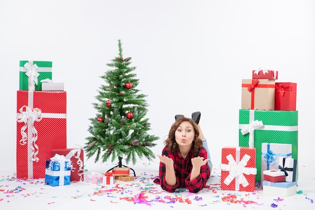 正面図クリスマスプレゼントと白い背景の上の休日の木の周りに横たわっている若い女性クリスマス新年の贈り物色雪